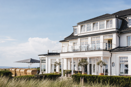 Hochwertige Außenaufnahme eines Hotels oder Restaurants in Küstennähe, ergänzt durch dezente digitale Geschäftselemente.